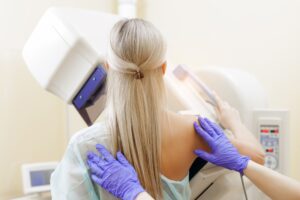 A technician in purple gloves helping a woman get into position for a mammogram screening.