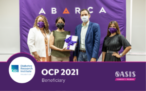 Four individuals wearing face masks stand in front of a purple Abarca backdrop, presenting a gift to a representative from the Diabetes Research Institute Foundation as part of the OCP 2021 Beneficiary recognition under the Oasis Community Program.