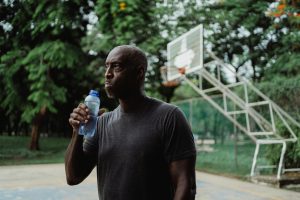 Middle-aged man drinking water after exercising on an outdoor basketball court, highlighting the importance of hydration and physical activity for men’s health.